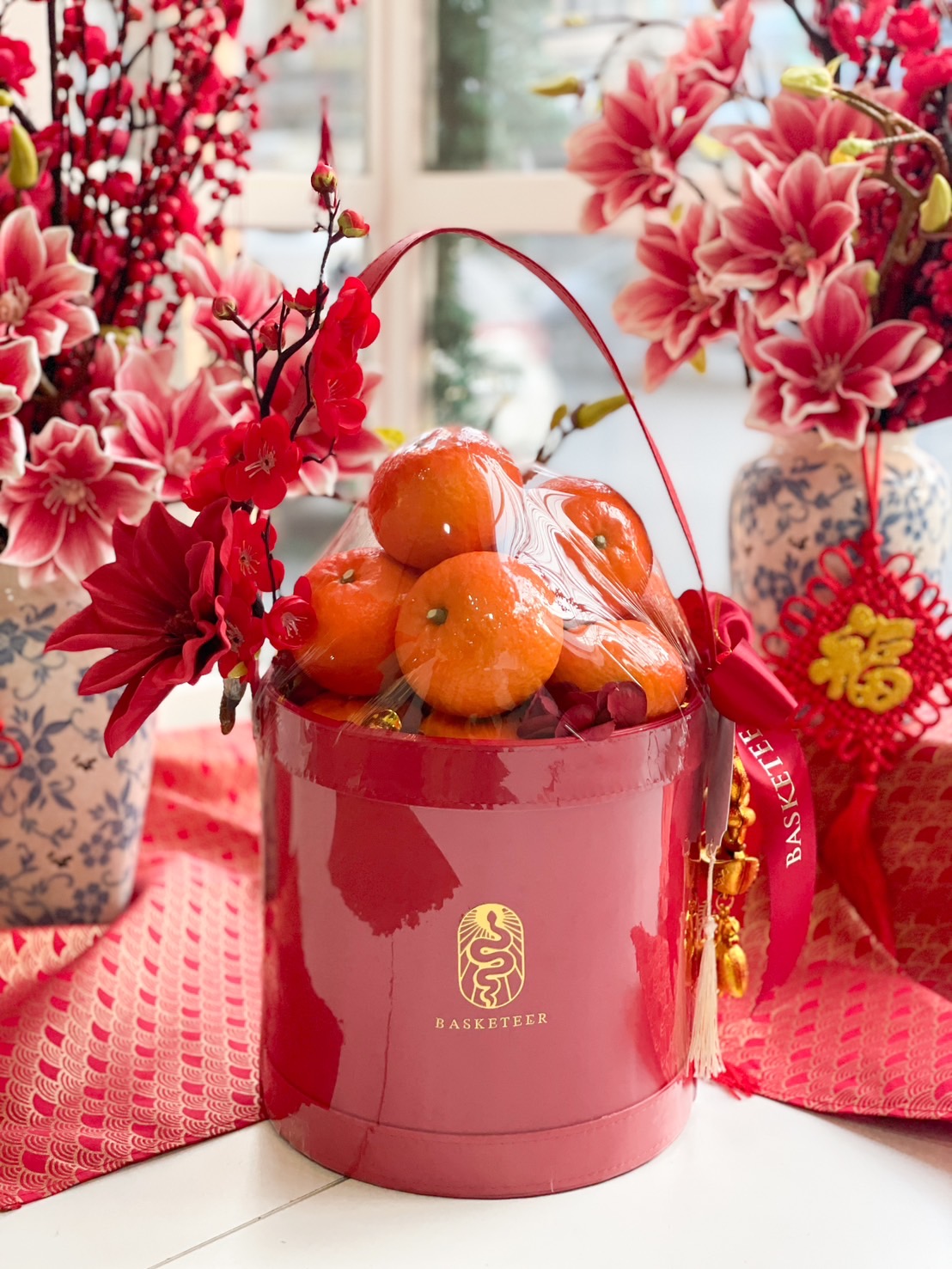 Elegant red Chinese New Year gift basket filled with fresh mandarin oranges, decorated with festive red flowers and lucky charms.