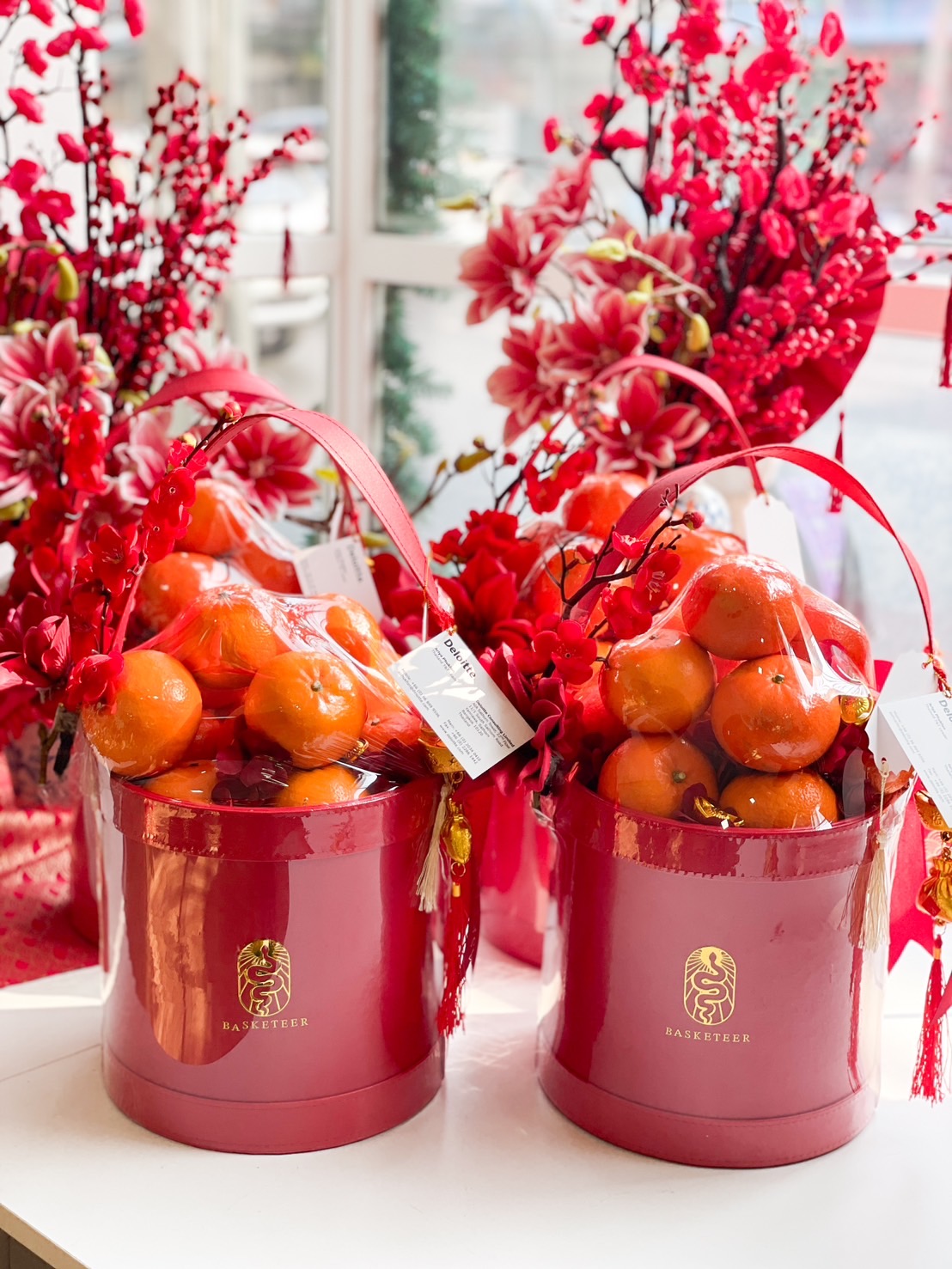 Elegant red Chinese New Year gift basket filled with fresh mandarin oranges, decorated with festive red flowers and lucky charms.
