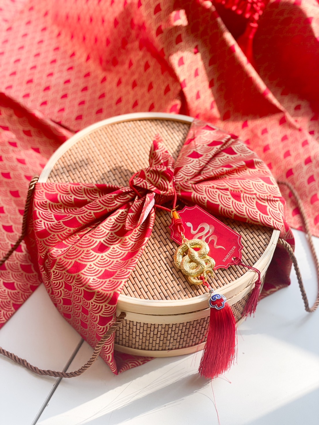 Chinese New Year bamboo gift basket with red and gold fabric wrapping, adorned with a golden snake charm and lucky tassels.