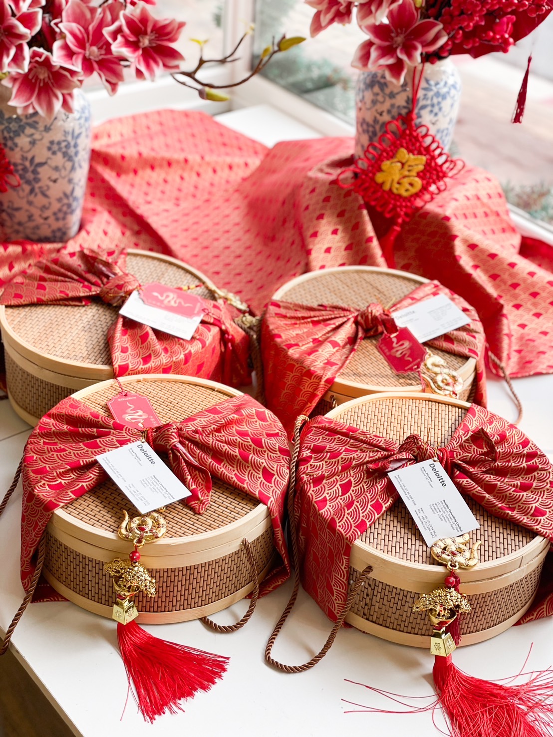 Premium Chinese New Year bamboo hamper set with woven gift boxes, red and gold fabric wrapping, and traditional prosperity charms.