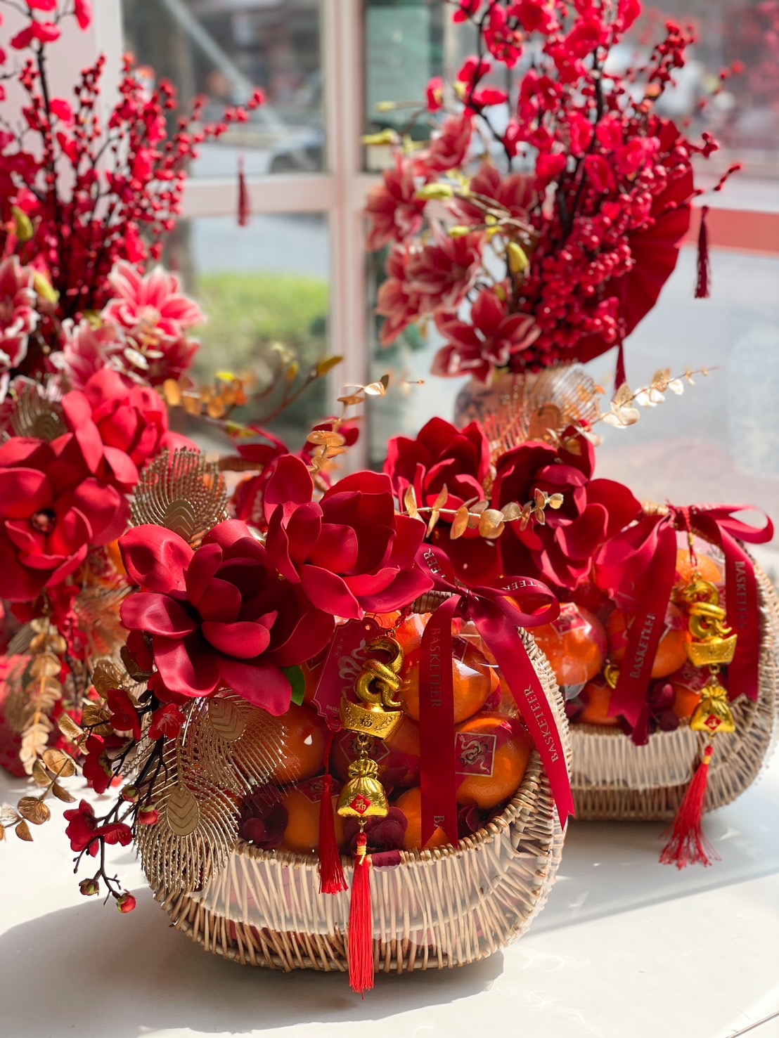 Luxury Chinese New Year fruit basket with Mandarin oranges, vibrant red flowers, gold decorations, and festive lucky charms.