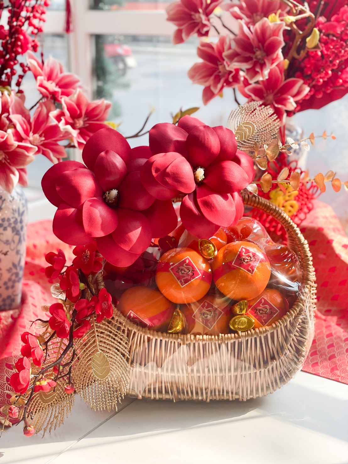 Elegant Chinese New Year fruit basket with Mandarin oranges, red floral decorations, gold accents, and traditional prosperity charms.