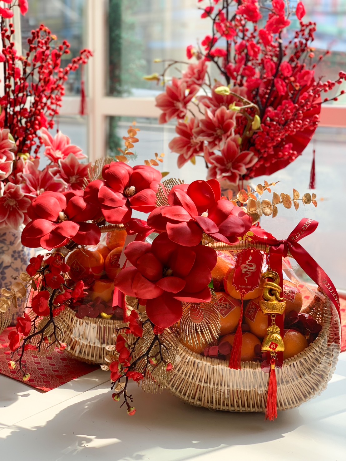 Luxury Chinese New Year fruit basket with Mandarin oranges, vibrant red flowers, gold decorations, and festive lucky charms.