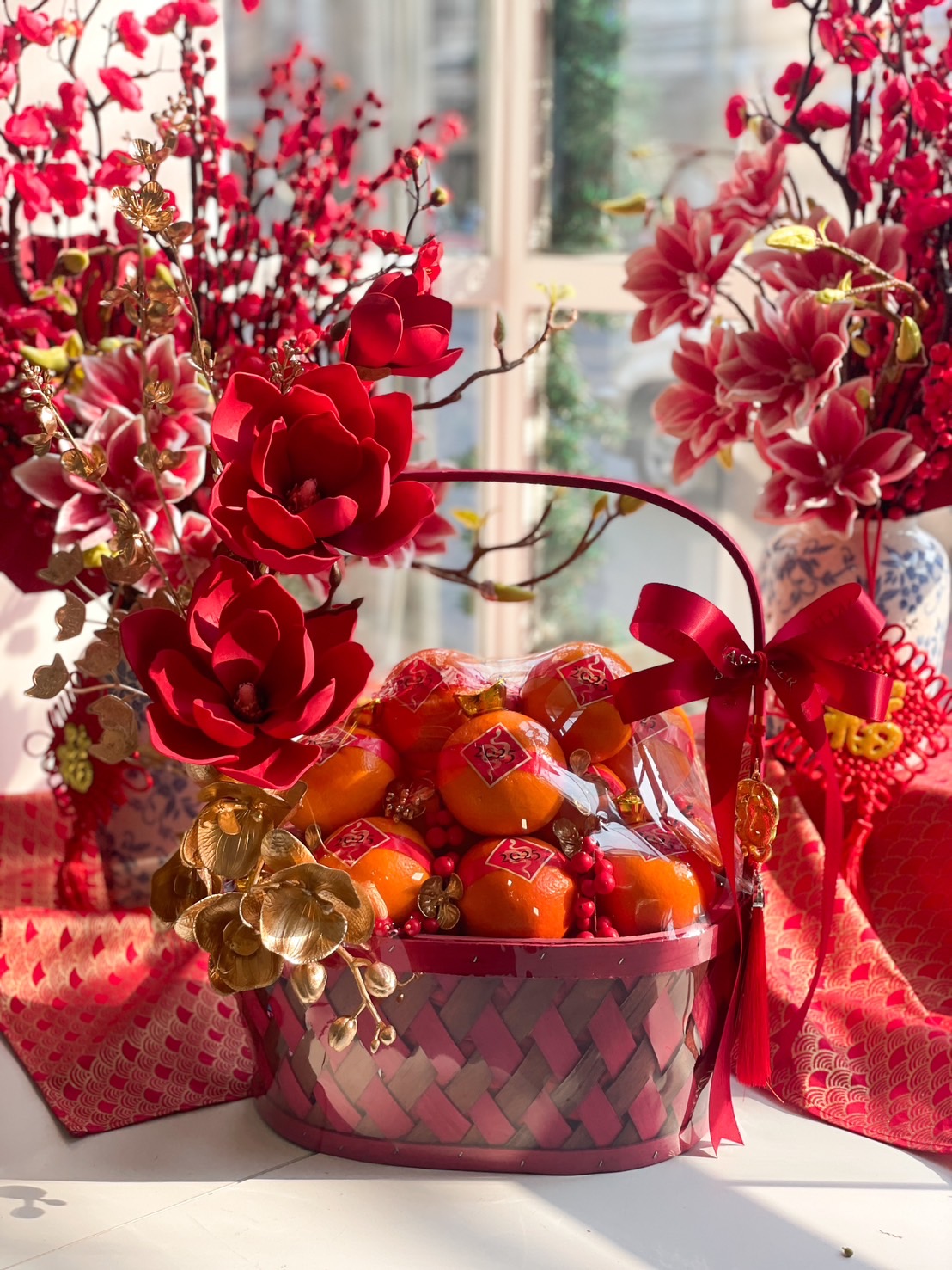 Luxury Chinese New Year prosperity basket with Mandarin oranges, red floral decorations, and gold accents for a festive and elegant celebration.