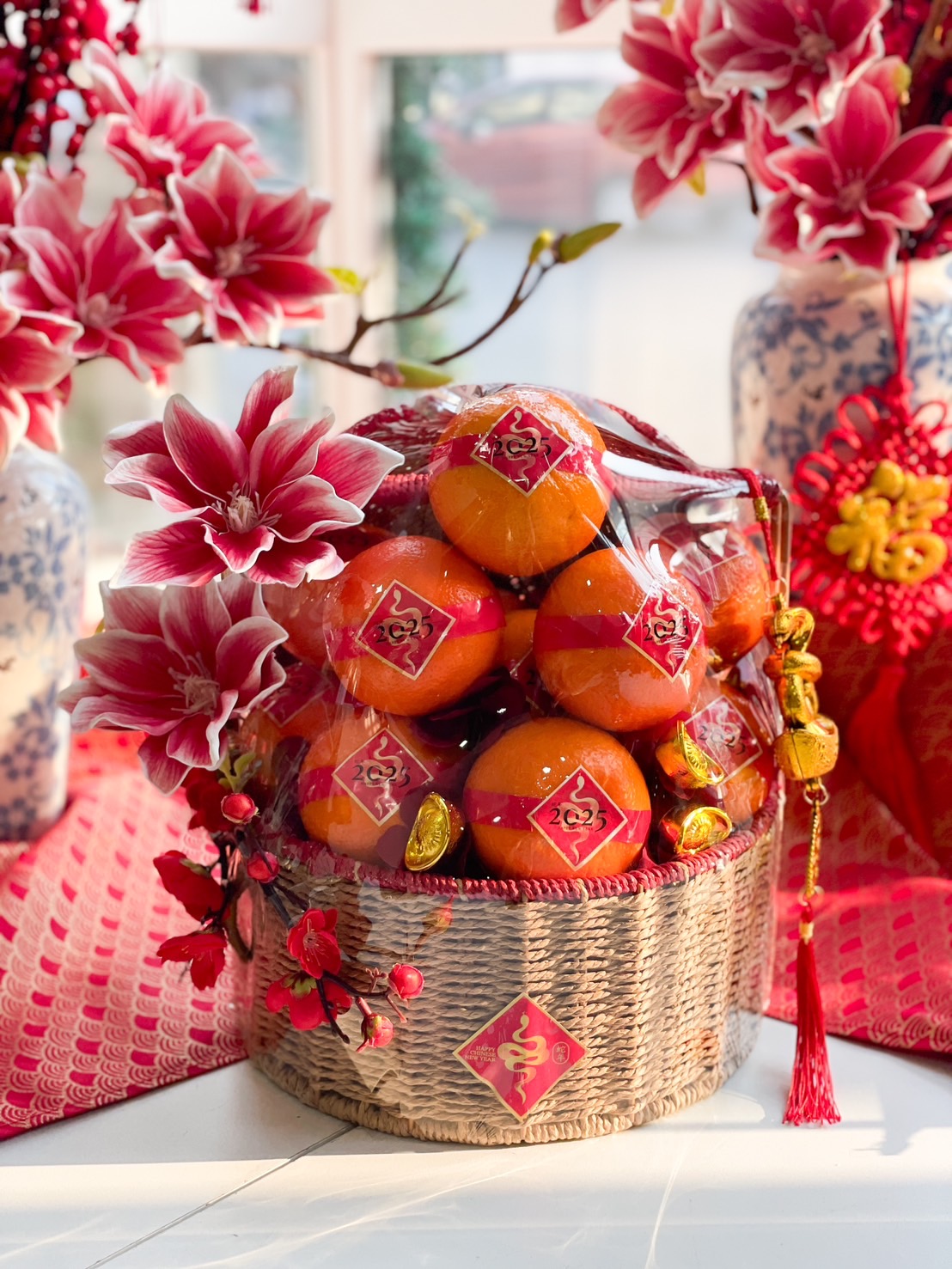 Chinese New Year prosperity basket with Mandarin oranges, festive floral accents, gold ingots, and traditional red and gold decorations.