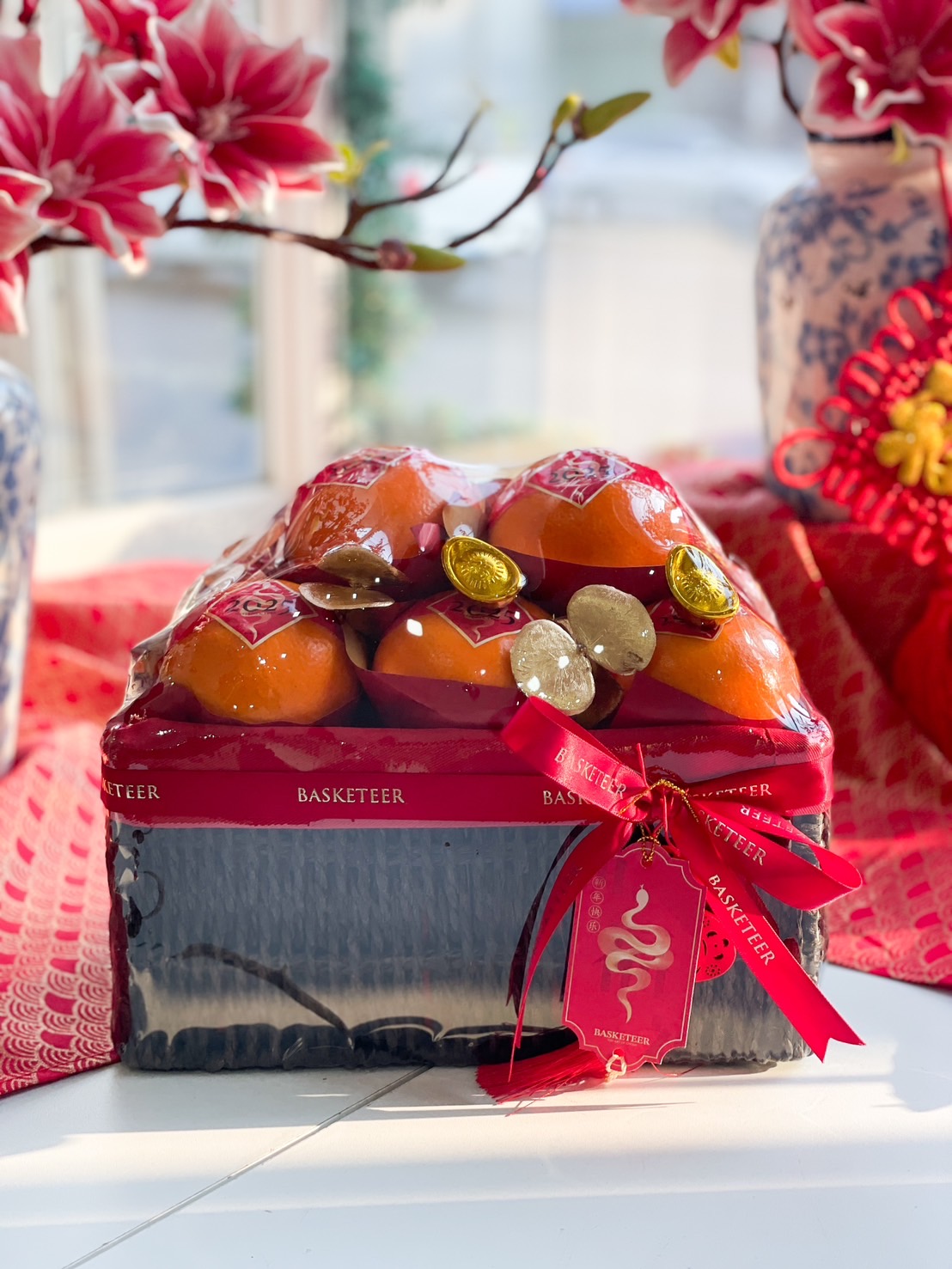 Elegant Chinese New Year Mandarin orange gift basket with fresh fruit, red ribbon, gold decorations, and prosperity charm for festive gifting.