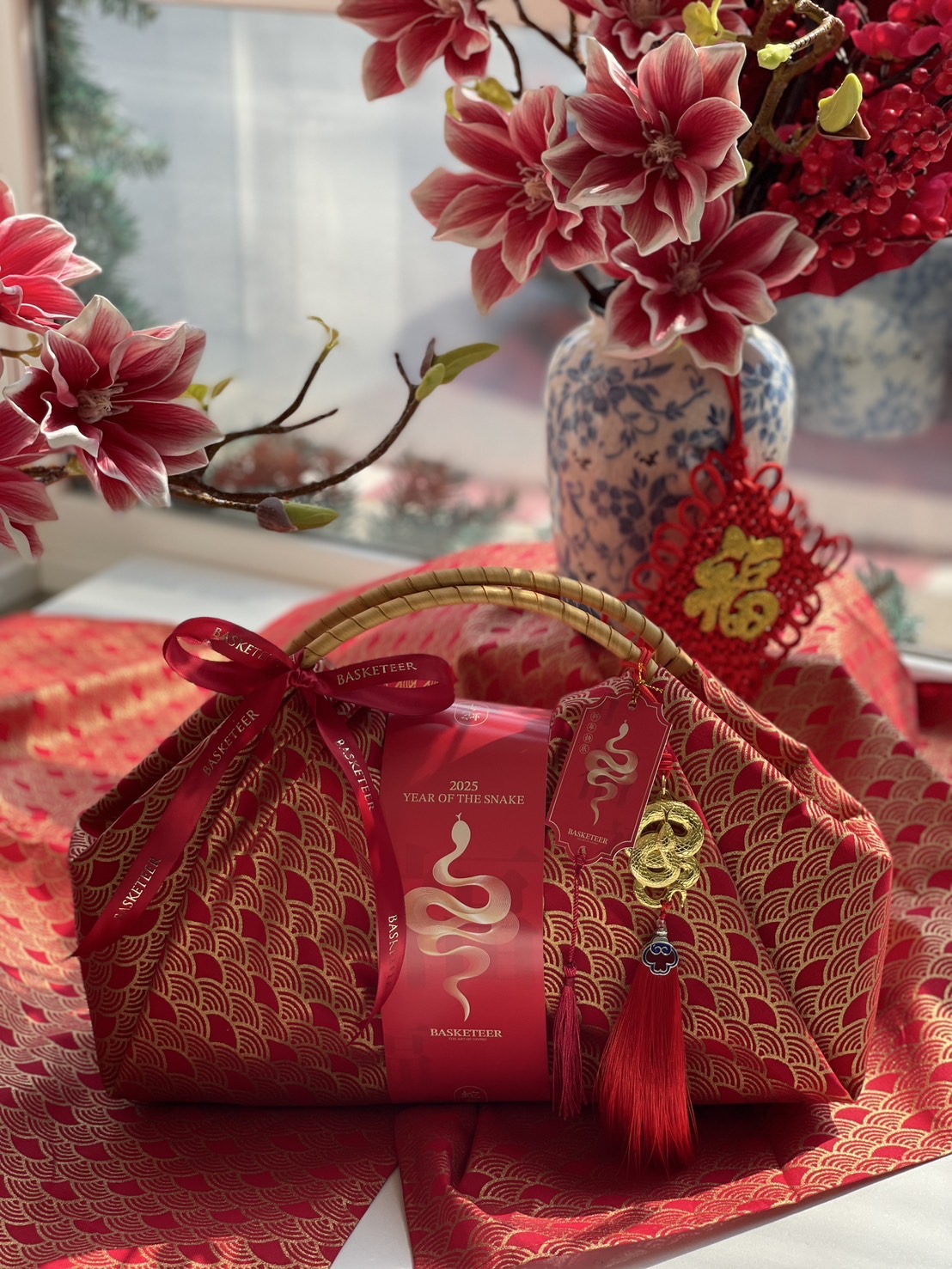 Luxury Chinese New Year fabric-wrapped hamper with red and gold design, bamboo handle, and festive prosperity charms for a sophisticated gift.