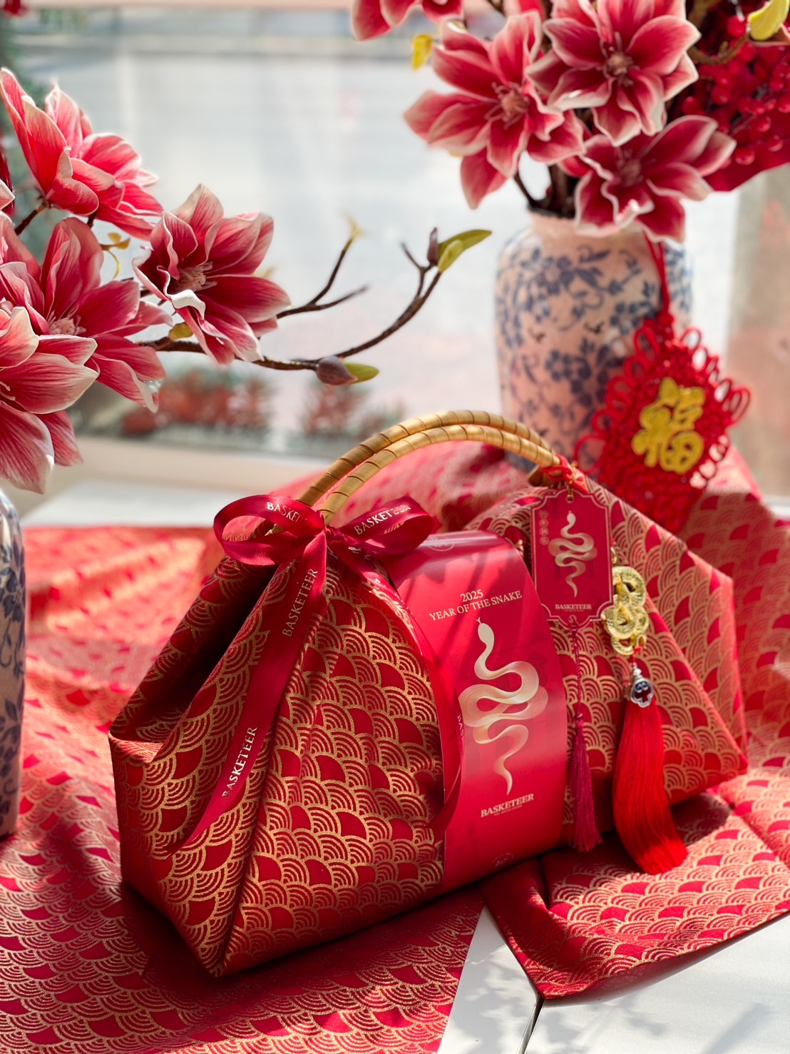 Luxury Chinese New Year fabric-wrapped hamper with red and gold design, bamboo handle, and festive prosperity charms for a sophisticated gift.