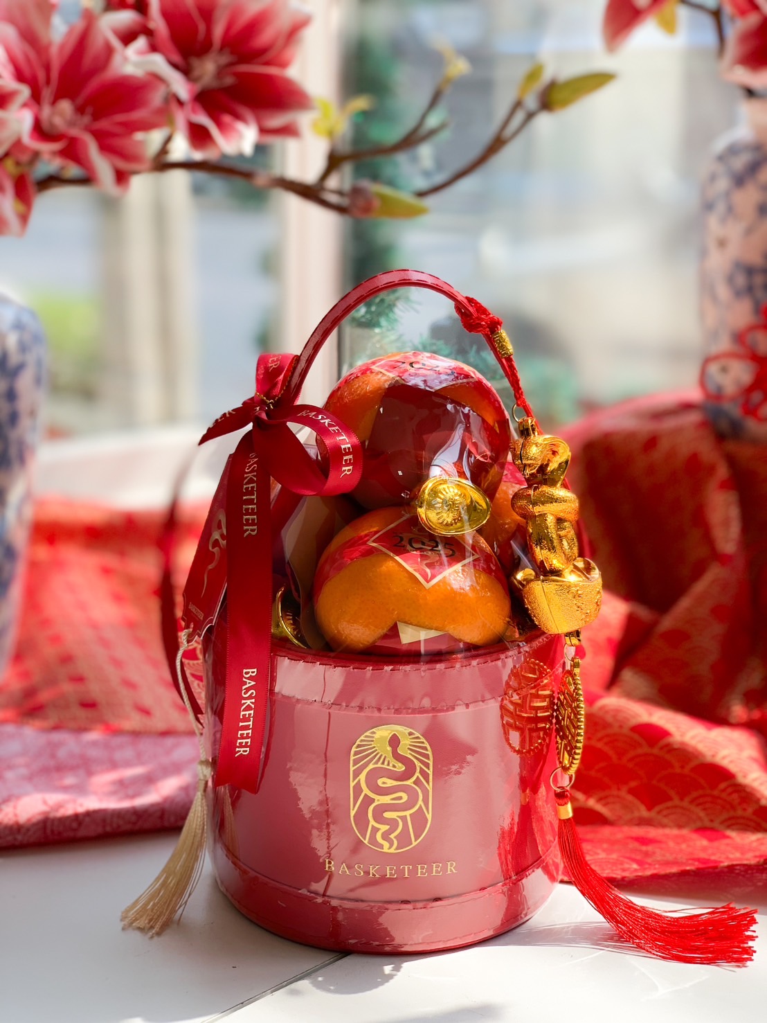 Red gift box featuring fresh mandarin oranges with gold accents and festive Chinese New Year decorations for the Year of the Snake.