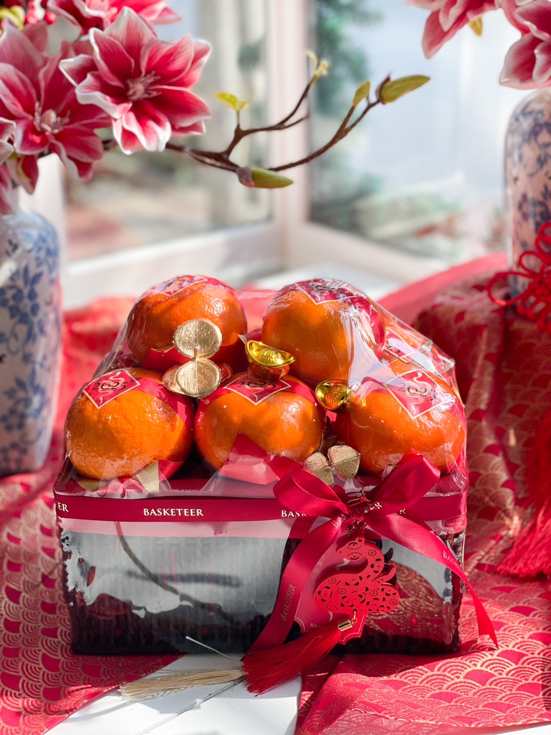 Elegant Chinese New Year Mandarin orange gift basket with fresh fruit, red ribbon, gold decorations, and prosperity charm for festive gifting.