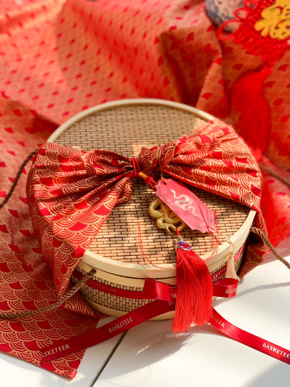 Luxury Chinese New Year bamboo hamper wrapped in red and gold fabric, with a woven bamboo box and festive lucky charm for prosperity.