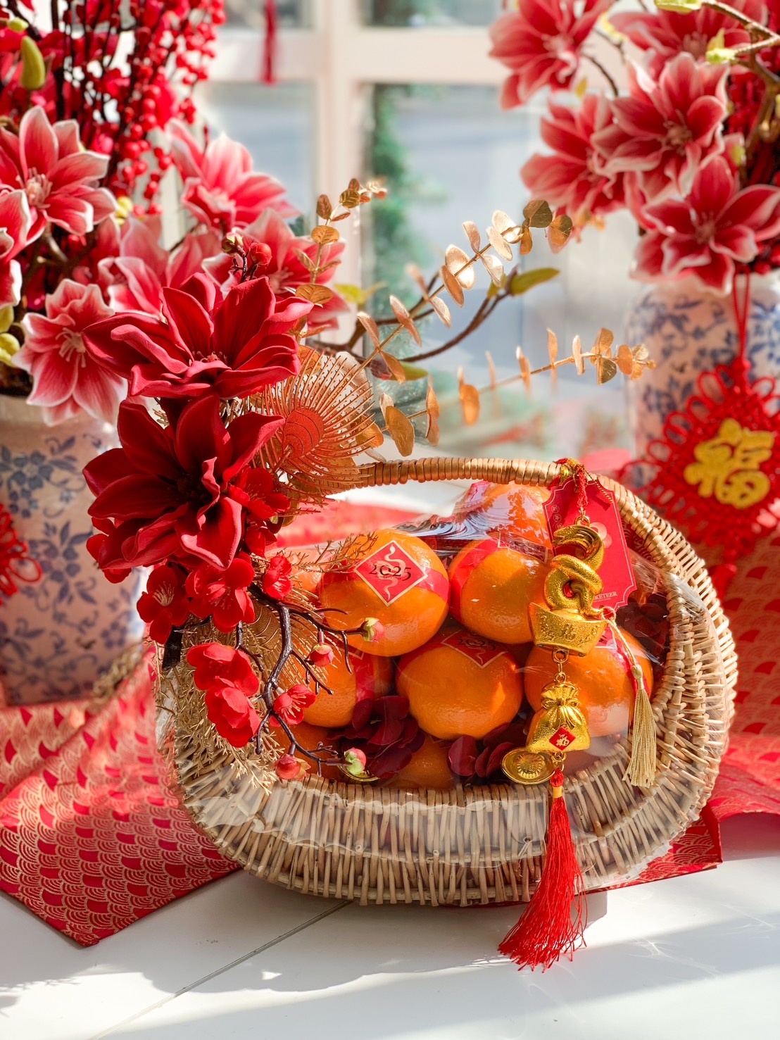 Elegant Chinese New Year fruit basket with Mandarin oranges, red floral decorations, gold accents, and traditional prosperity charms.