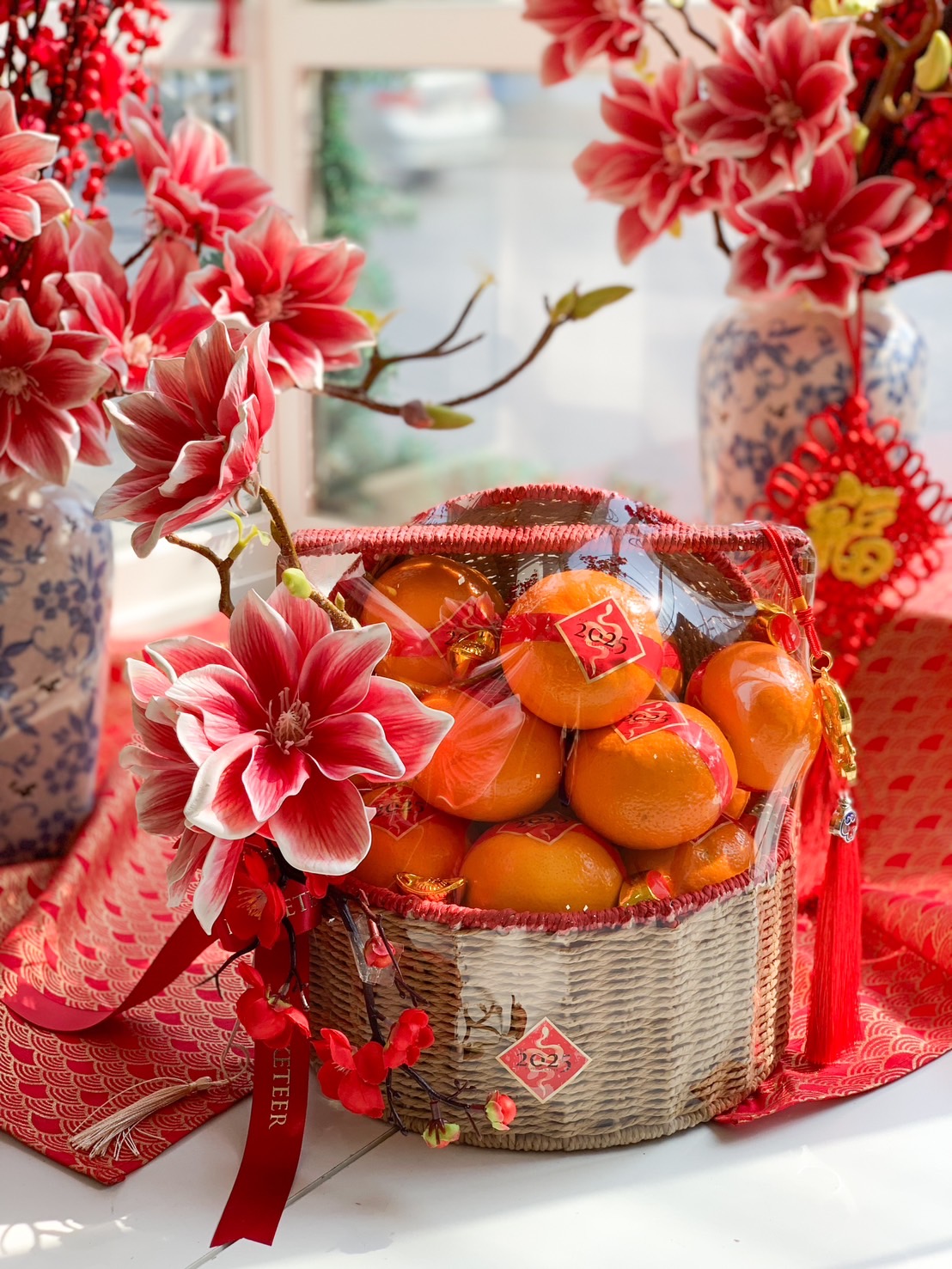 Chinese New Year prosperity basket with Mandarin oranges, festive floral accents, gold ingots, and traditional red and gold decorations.