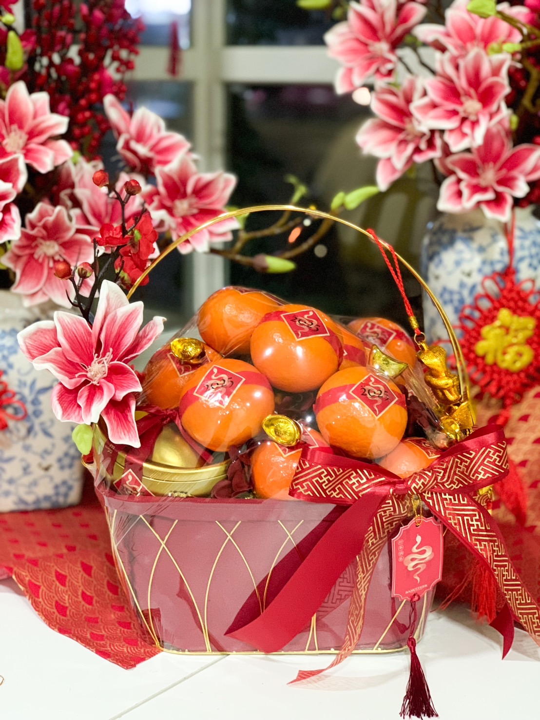 Luxury Chinese New Year fruit basket with Mandarin oranges, gold ingots, festive red ribbon, and floral decorations for prosperity and luck.