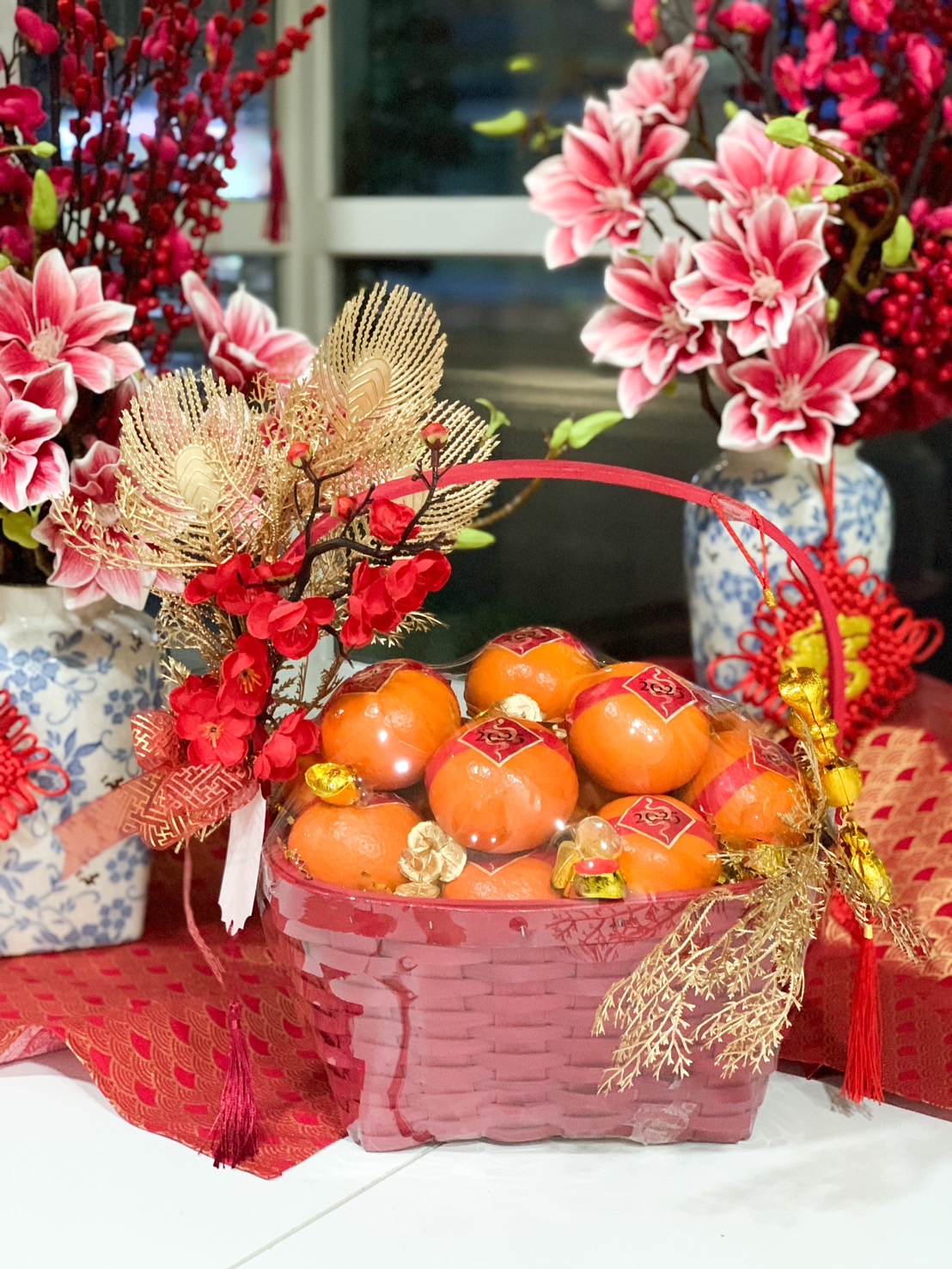 Red Chinese New Year gift basket filled with fresh mandarins, adorned with gold decorations and vibrant red festive accents.