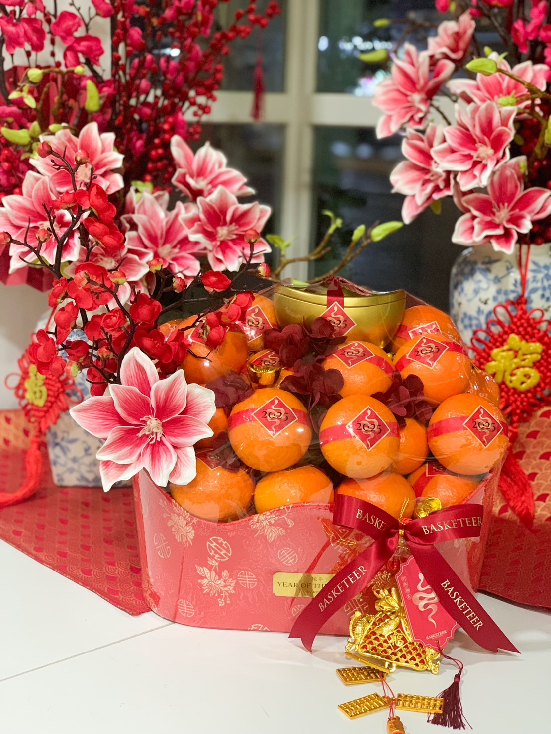 Deluxe Chinese New Year gift basket with fresh Mandarin oranges, festive red packaging, gold ingot decoration, and elegant floral accents.