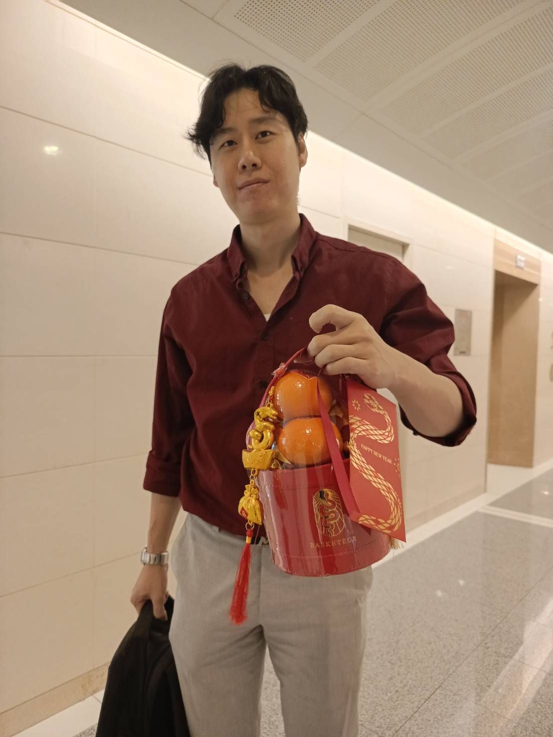 Chinese New Year prosperity gift bucket with mandarin oranges, gold charms, red ribbons, and tassels for luck and wealth.