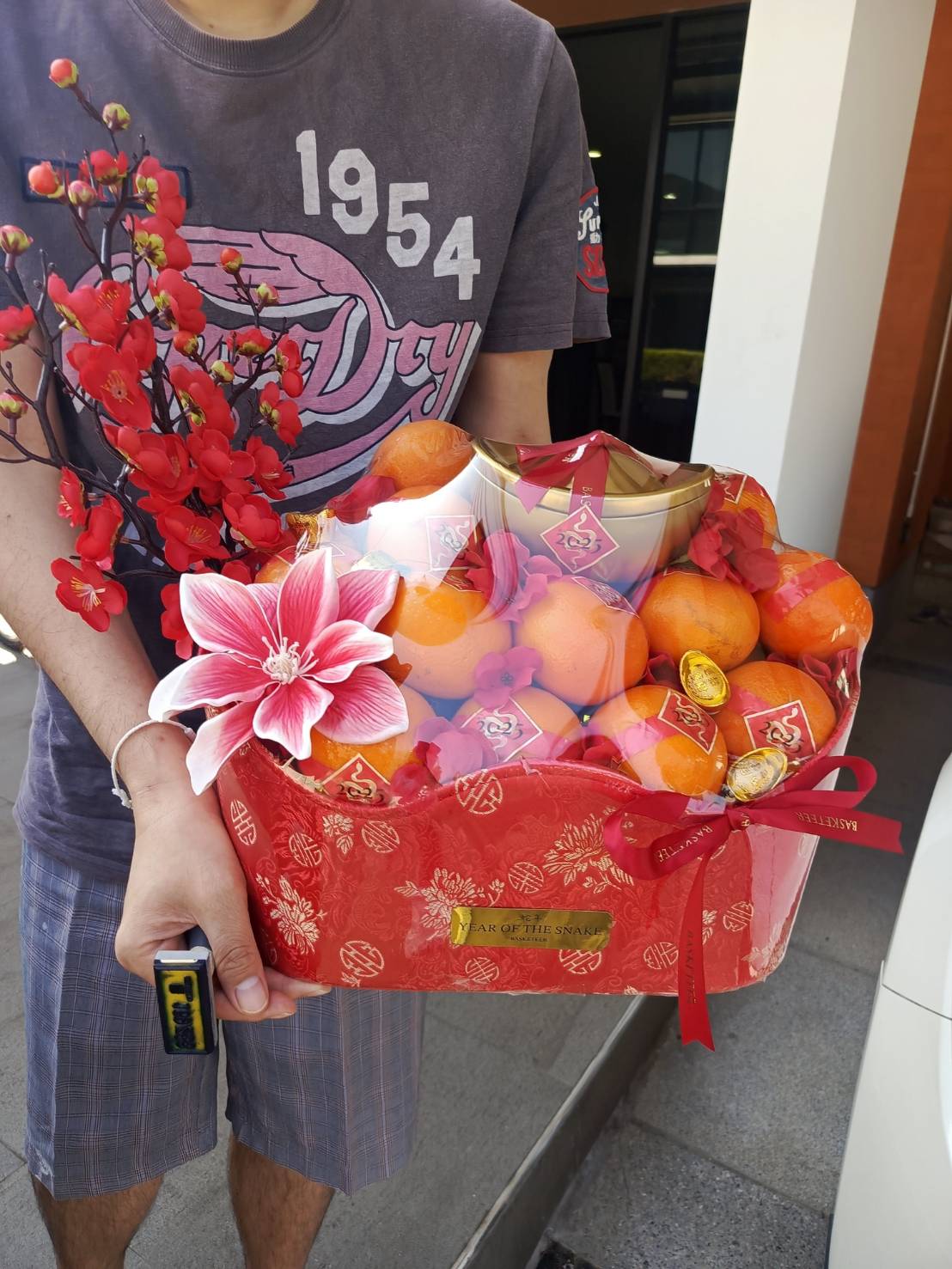 Chinese New Year gift basket with mandarin oranges, gold ingots, a decorative golden bowl, and red floral accents for good luck.