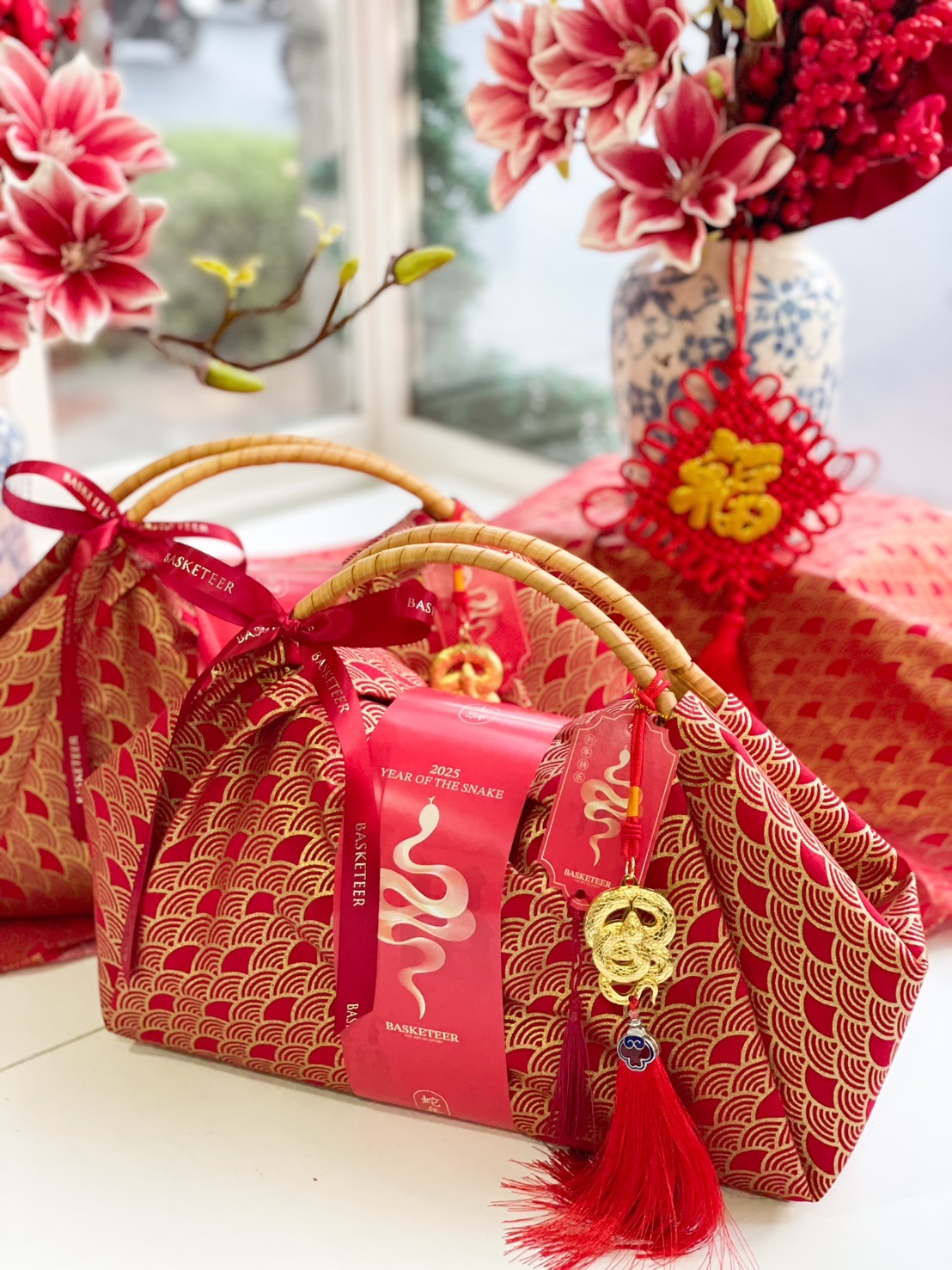 Chinese New Year gift bundle wrapped in red and gold fabric with a bamboo handle, festive tassels, and gold charms for good luck.