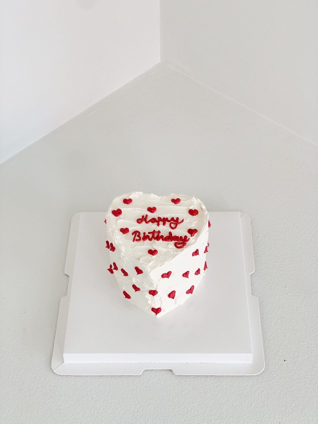 Small heart-shaped birthday cake with white cream and red mini heart decorations.