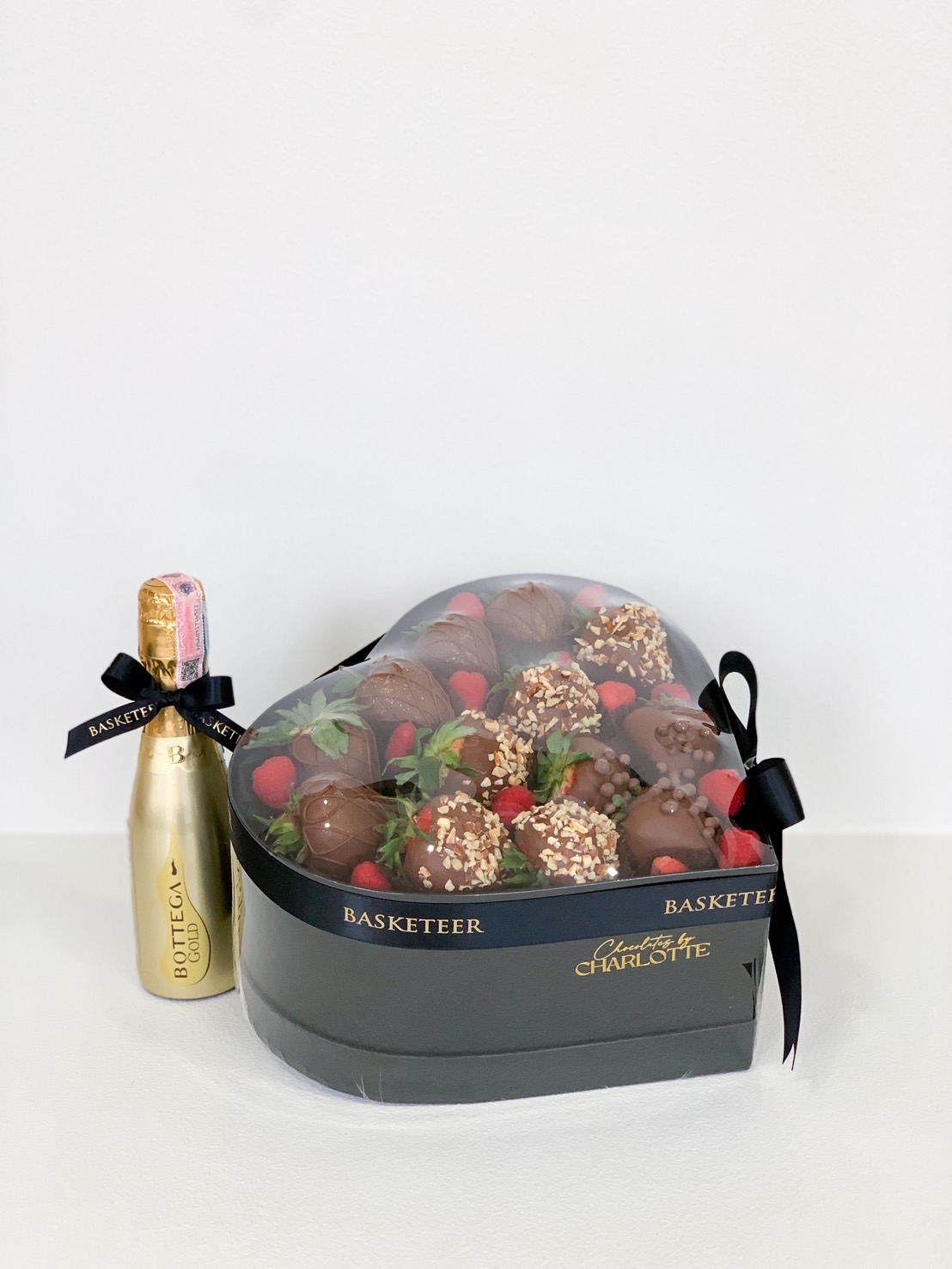 Heart-shaped black gift box of chocolate dipped strawberries and raspberries with mini Bottega Gold prosecco bottle.