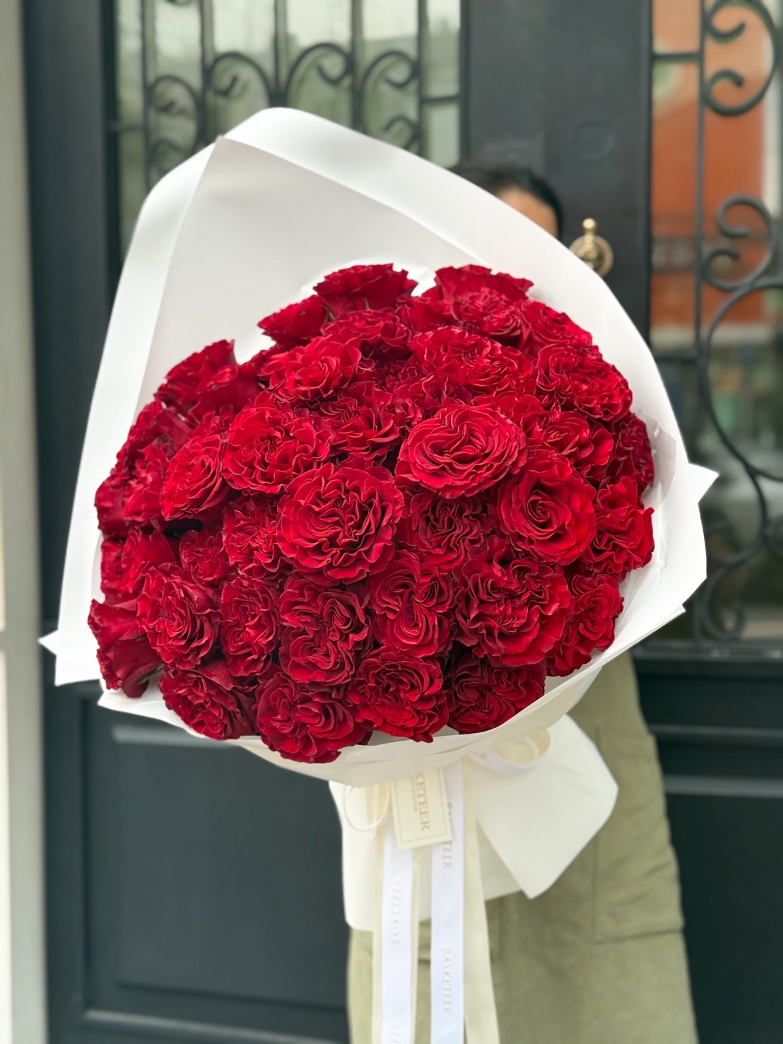 Large luxury bouquet of premium red roses with layered petals, wrapped in elegant white paper with satin Basketeer ribbon.