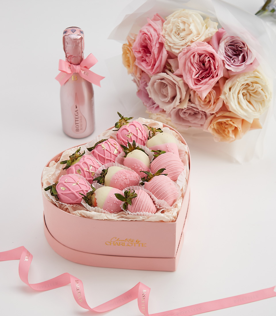 Heart-shaped gift box with pink and white chocolate-covered strawberries, gold accents, and a bottle of sparkling rosé.