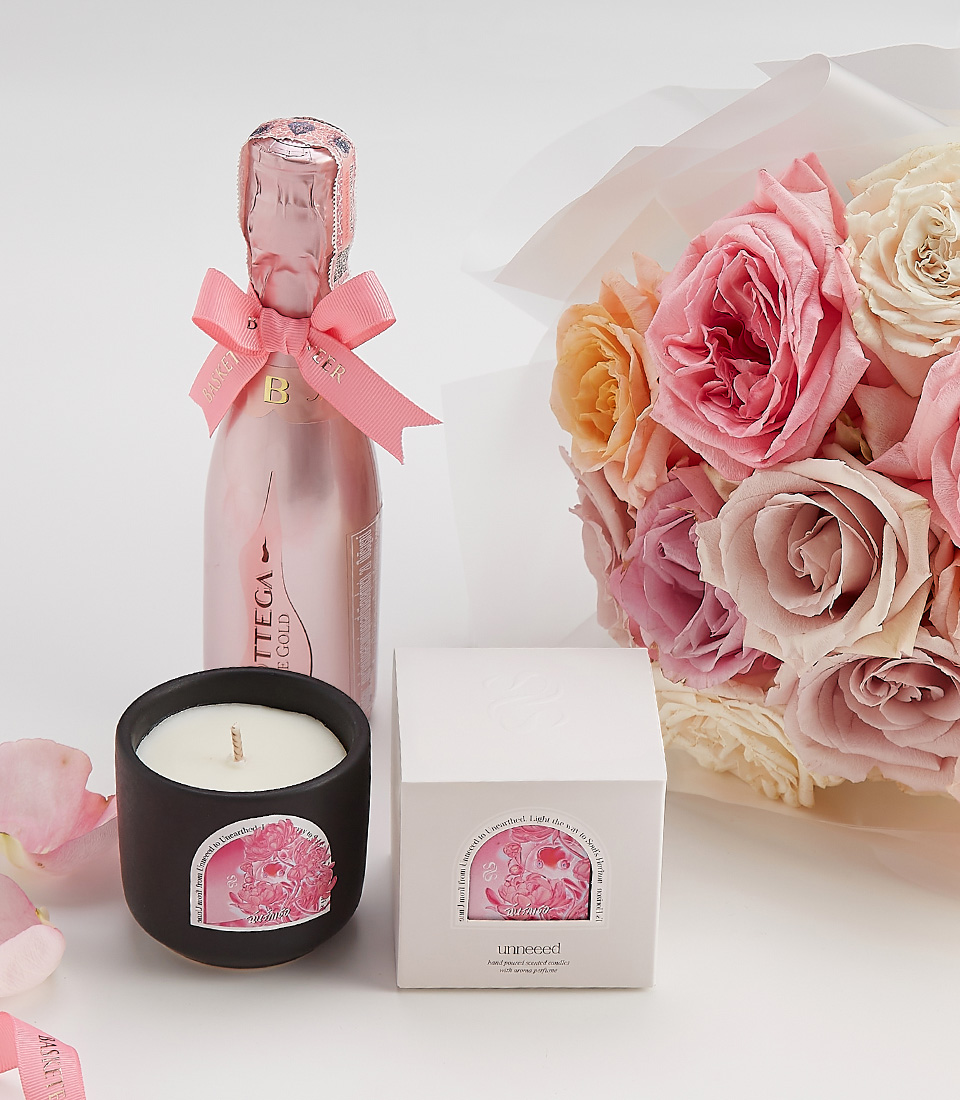 Close-up of a Blush rose bouquet with a scented candle and sparkling wine – a romantic gift set.