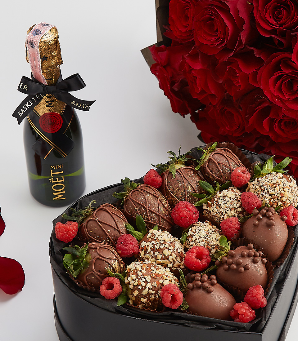 Luxury heart-shaped chocolate strawberry gift box with Moët champagne and a bouquet of red roses.
