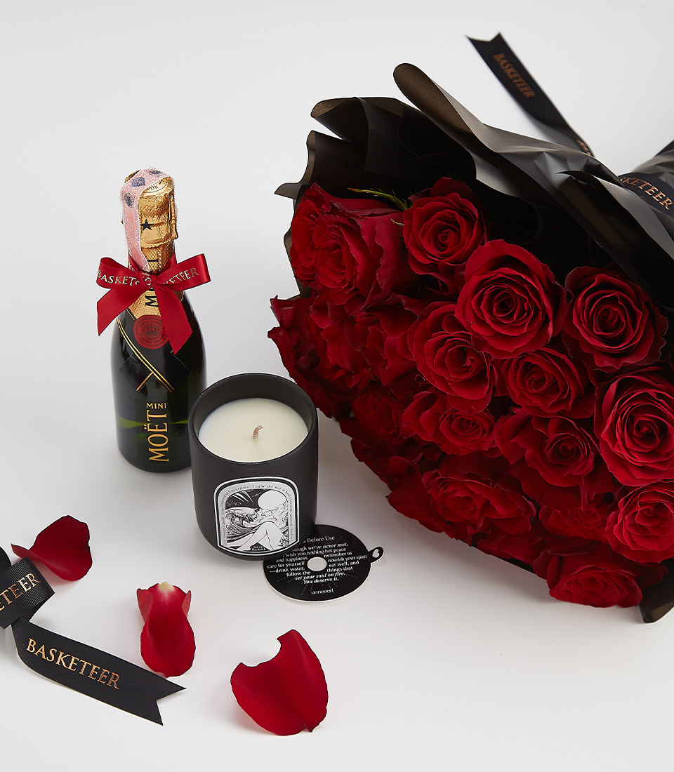 A premium romantic gift set including a bouquet of deep red roses, a mini Moët champagne bottle, and a black luxury scented candle, elegantly arranged with rose petals and a black Basketeer ribbon.