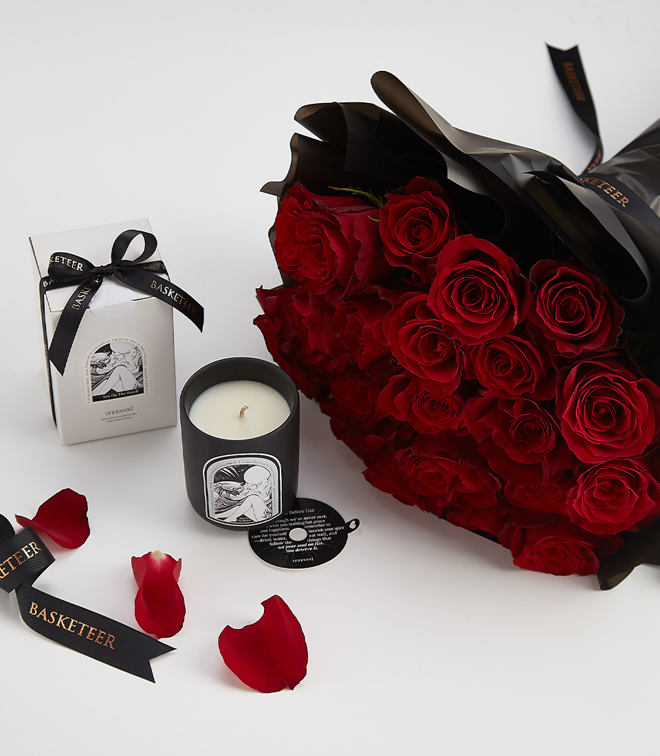 A luxurious romantic gift set featuring a bouquet of deep red roses, a black luxury scented candle, and an elegant Basketeer ribbon, designed for special occasions.