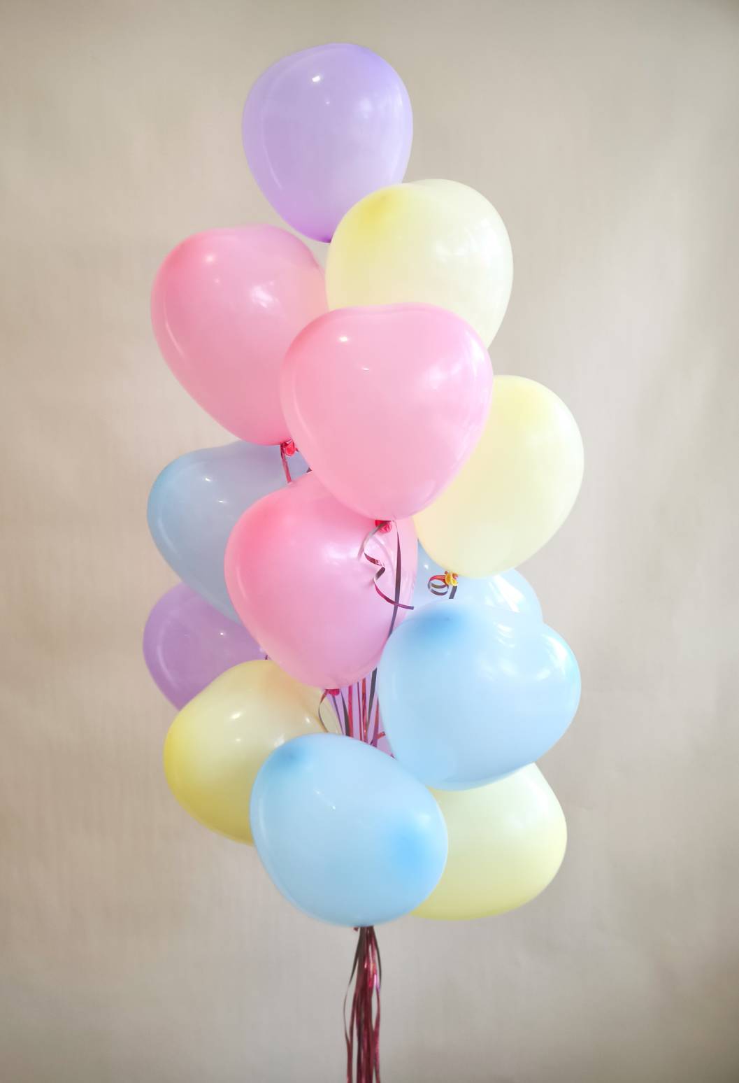 Pastel balloon bouquet with heart-shaped balloons in pink, blue, yellow, and purple tones tied together with red ribbon.