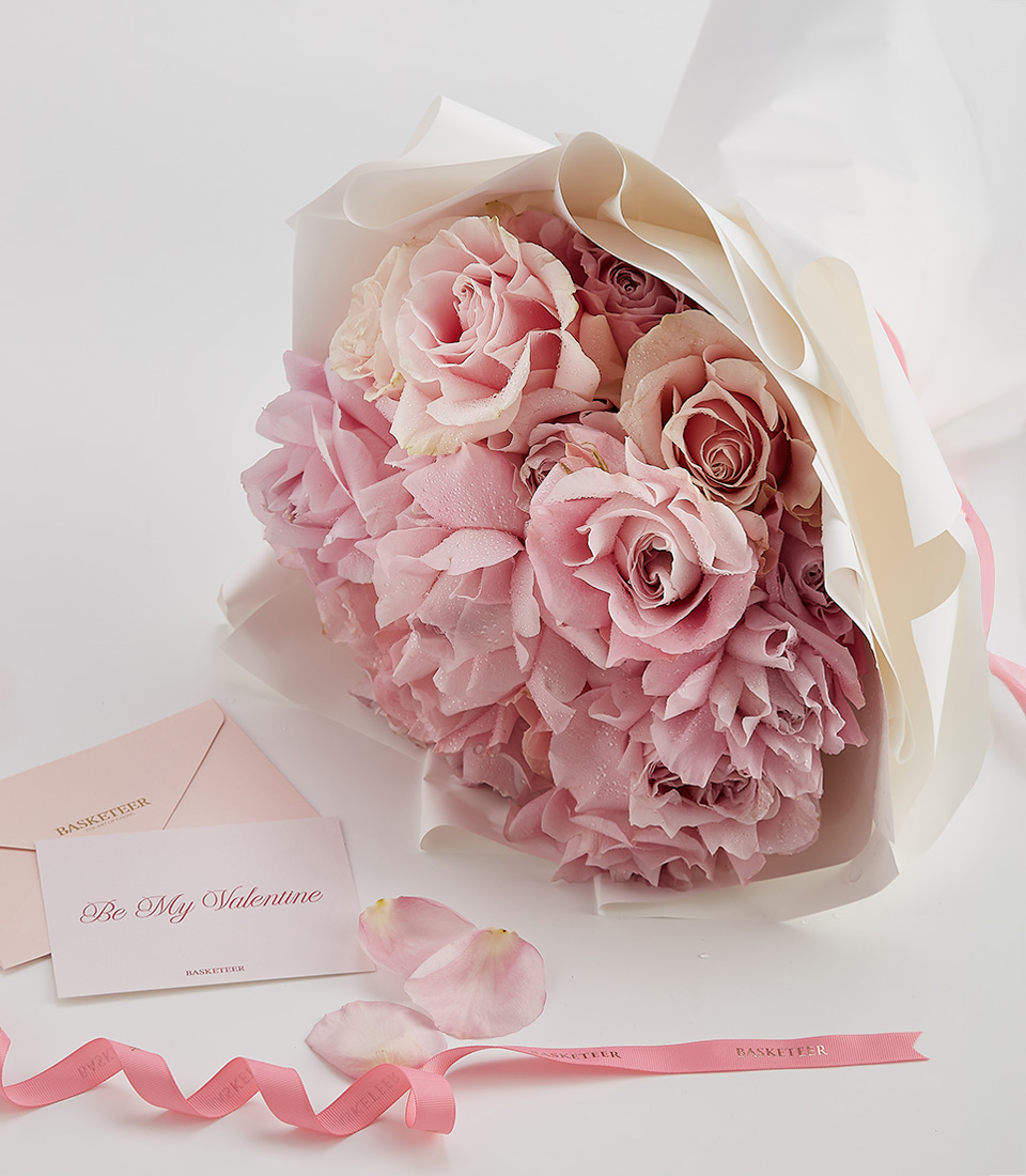 A beautifully arranged bouquet of soft pink roses, wrapped in elegant white paper with a Be My Valentine card and pink ribbon.