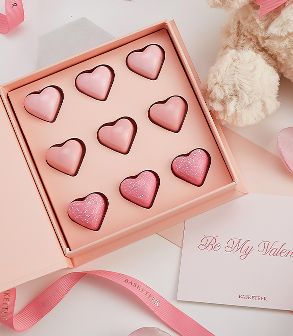 Close-up of a romantic Valentine’s gift with a plush teddy bear, pink heart chocolates, Bottega Rose Gold Champagne, and a heartfelt greeting card.