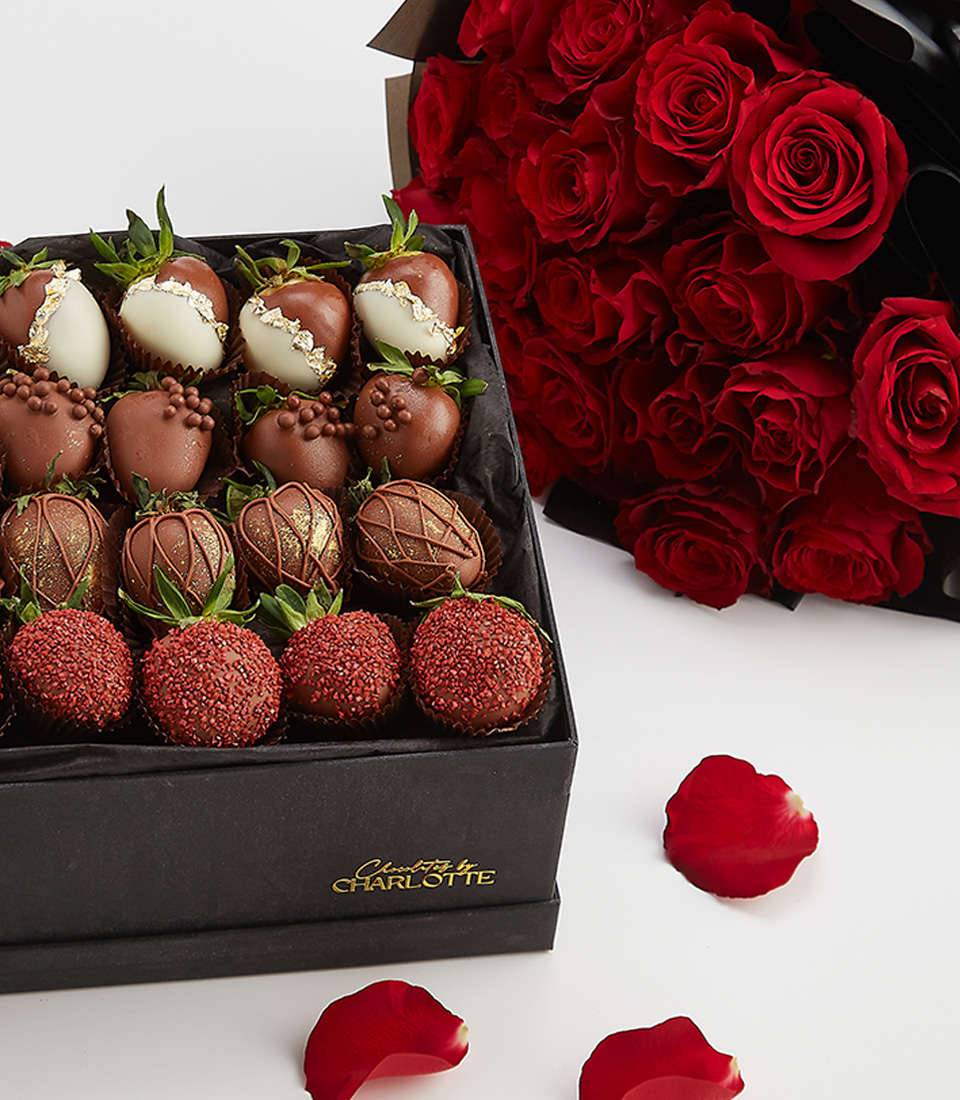 Close-up of a premium black gift box of chocolate-dipped strawberries, accompanied by a bouquet of red roses, elegantly arranged for a romantic gift.