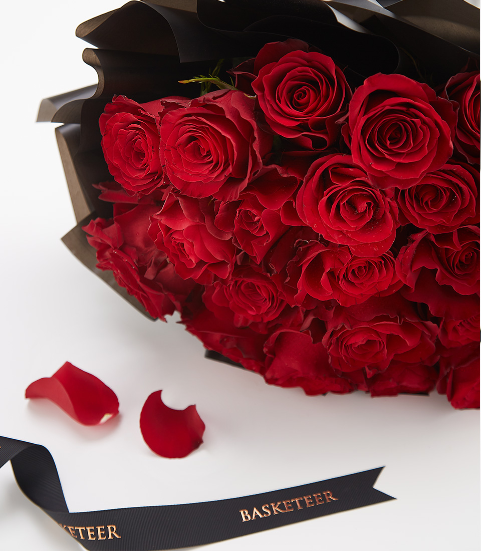 Close-up of a luxurious bouquet of 20 deep red roses, elegantly wrapped in black with a Basketeer ribbon.