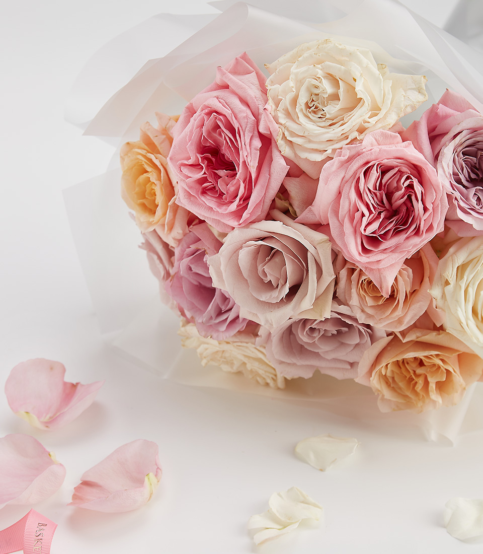 Close-up of a stunning bouquet of pastel roses in shades of pink, ivory, and peach, wrapped in elegant white paper with a Basketeer ribbon.