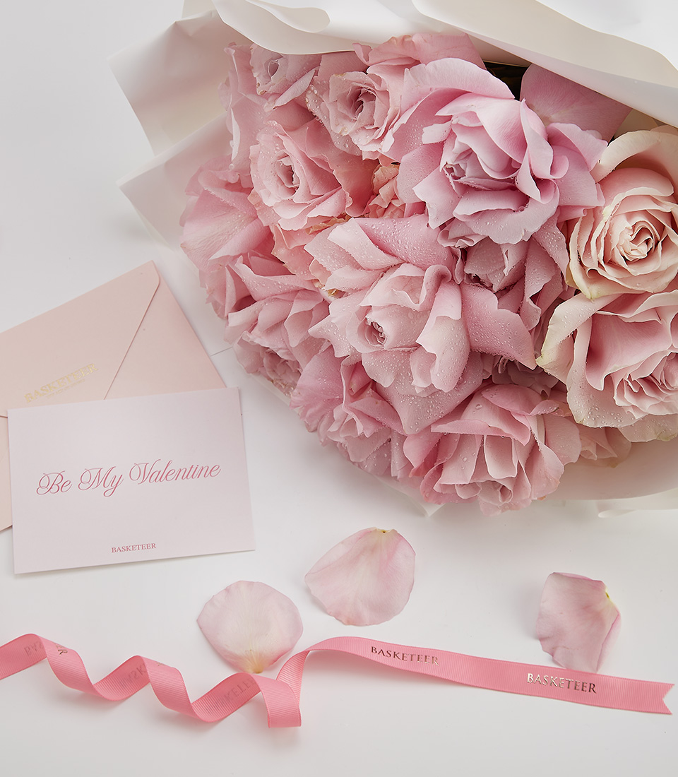 Close-up of a beautifully arranged bouquet of soft pink roses, wrapped in elegant white paper with a Be My Valentine card and pink ribbon.