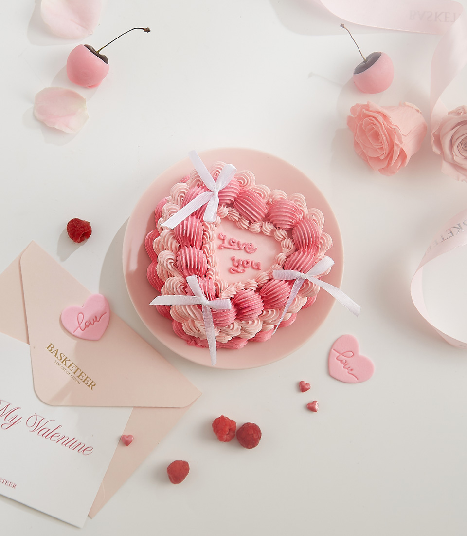 A beautiful pink heart-shaped cake with piped buttercream swirls, white bows, and 