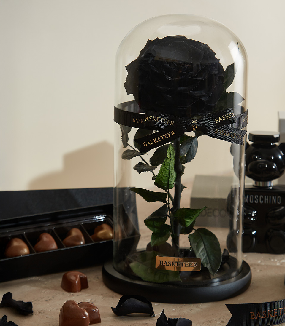 Close-up of a luxurious gift set featuring a black preserved rose under a glass dome, designer fragrances, handcrafted chocolates, and an elegant black candle—ideal for a stylish and meaningful gift.