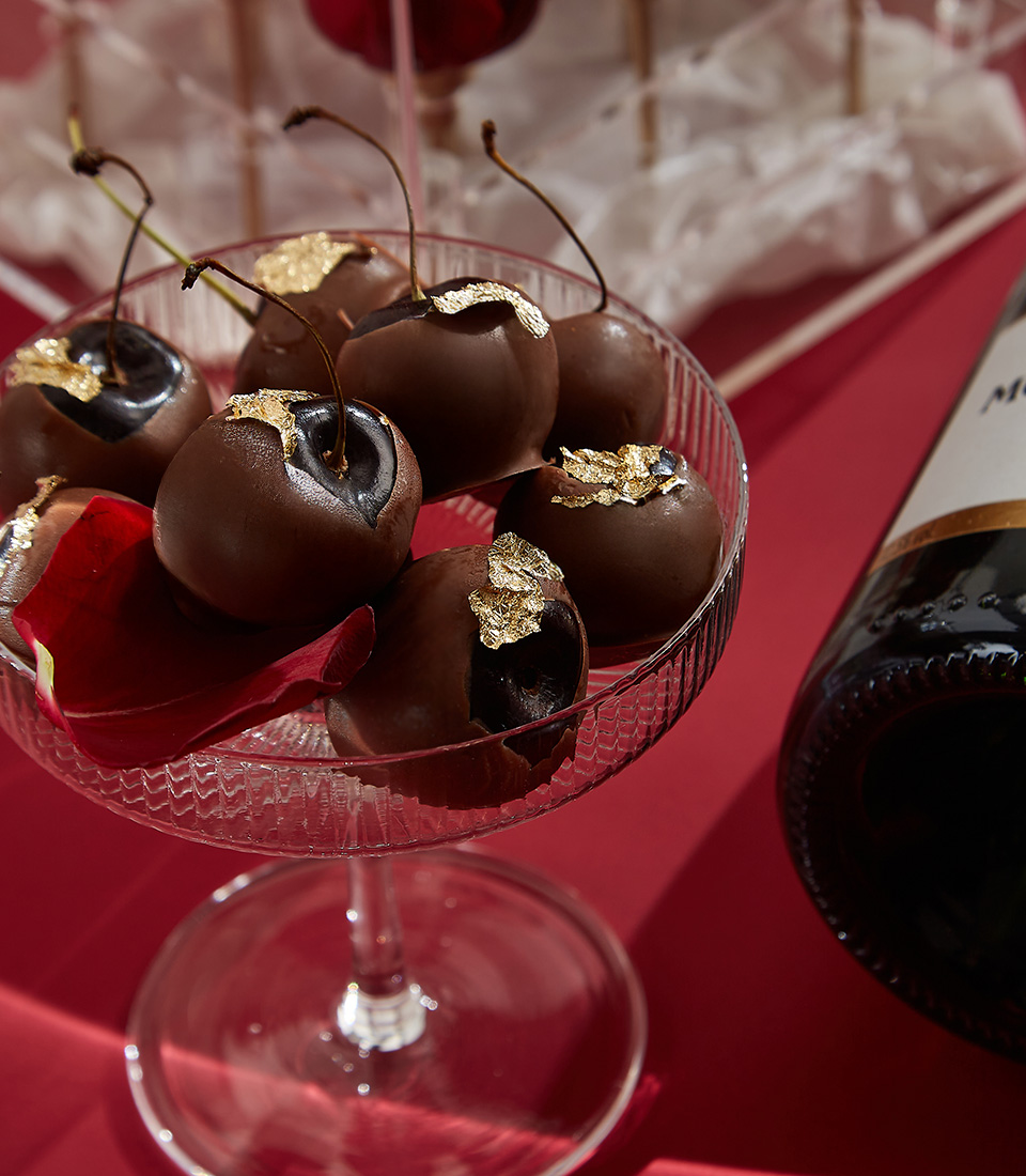 Close-up of a luxurious Valentine's gift set featuring Moët & Chandon Brut champagne, red preserved roses in an acrylic box, Moschino Toy Boy perfume, gold-accented chocolates, and a scented candle—the ultimate romantic gesture.