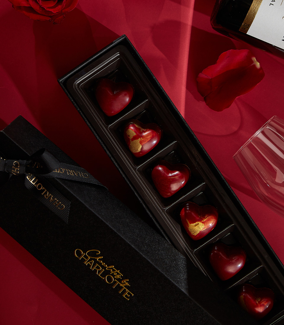 Close-up of a luxurious Valentine's gift set featuring Moët & Chandon Brut champagne, red preserved roses in an acrylic box, Moschino Toy Boy perfume, gold-accented chocolates, and a scented candle—the ultimate romantic gesture.