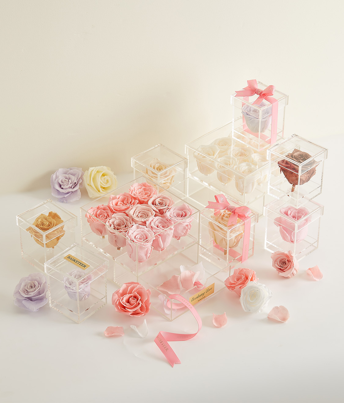 A collection of luxury preserved roses in clear acrylic boxes, featuring pink, white, and gold roses with elegant ribbons and branding