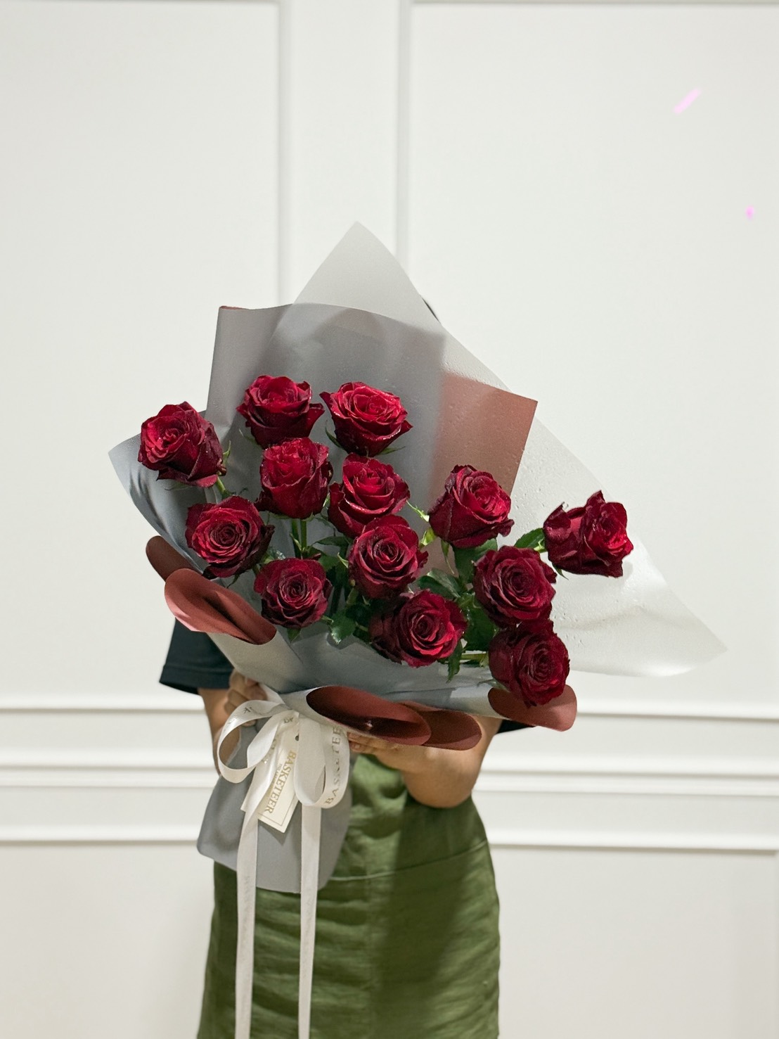 A woman in an emerald dress presents a Scarlet Elegance Red Rose Bouquet, exquisitely wrapped with ribbon, in Bangkok.