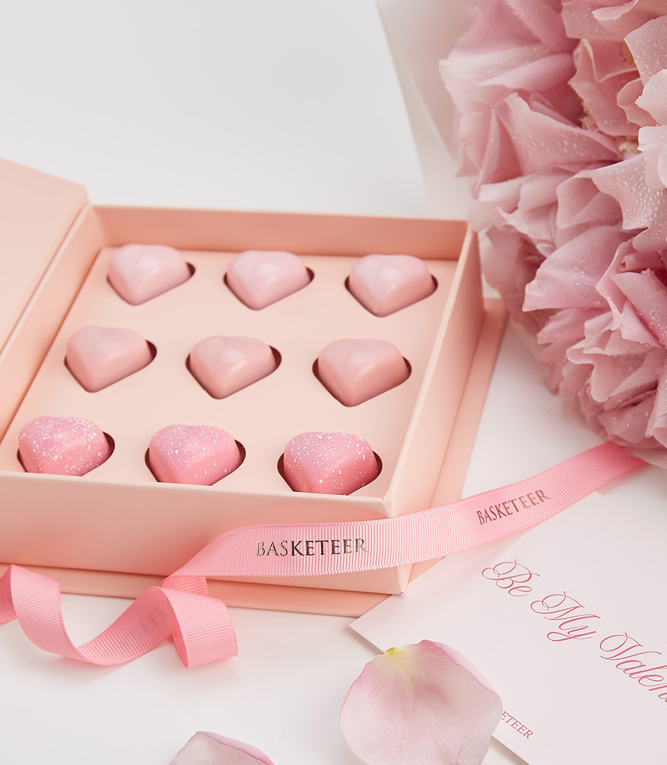 A luxurious Valentine's gift featuring a box of heart-shaped pink chocolates and a bouquet of soft pink roses.