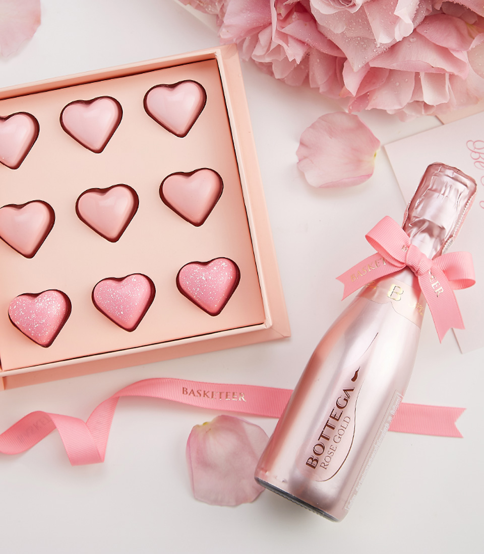 A Valentine’s Day gift set featuring Bottega Rose Gold Sparkling Wine, heart-shaped chocolates, and a bouquet of pink roses.