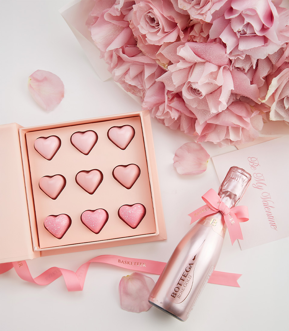 A Valentine’s Day gift set featuring Bottega Rose Gold Sparkling Wine, heart-shaped chocolates, and a bouquet of pink roses.