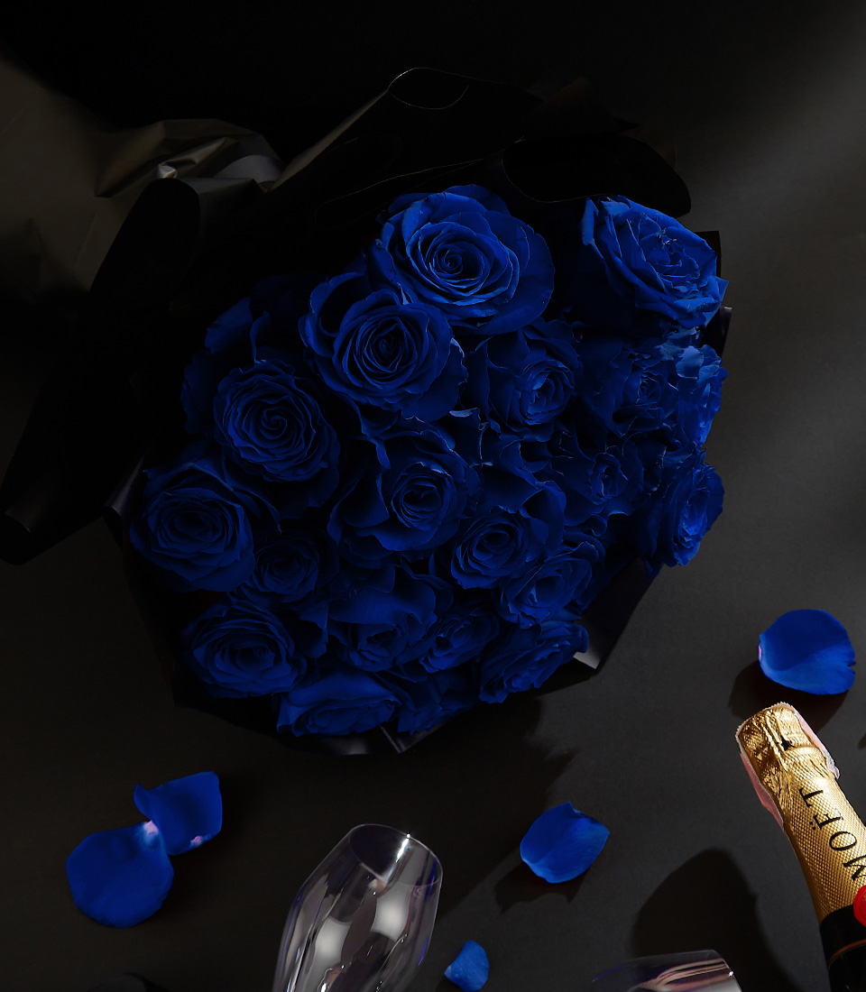 Moët & Chandon champagne bottle with two crystal flutes, surrounded by royal blue roses and petals on a black background, with a Basketeer ribbon.