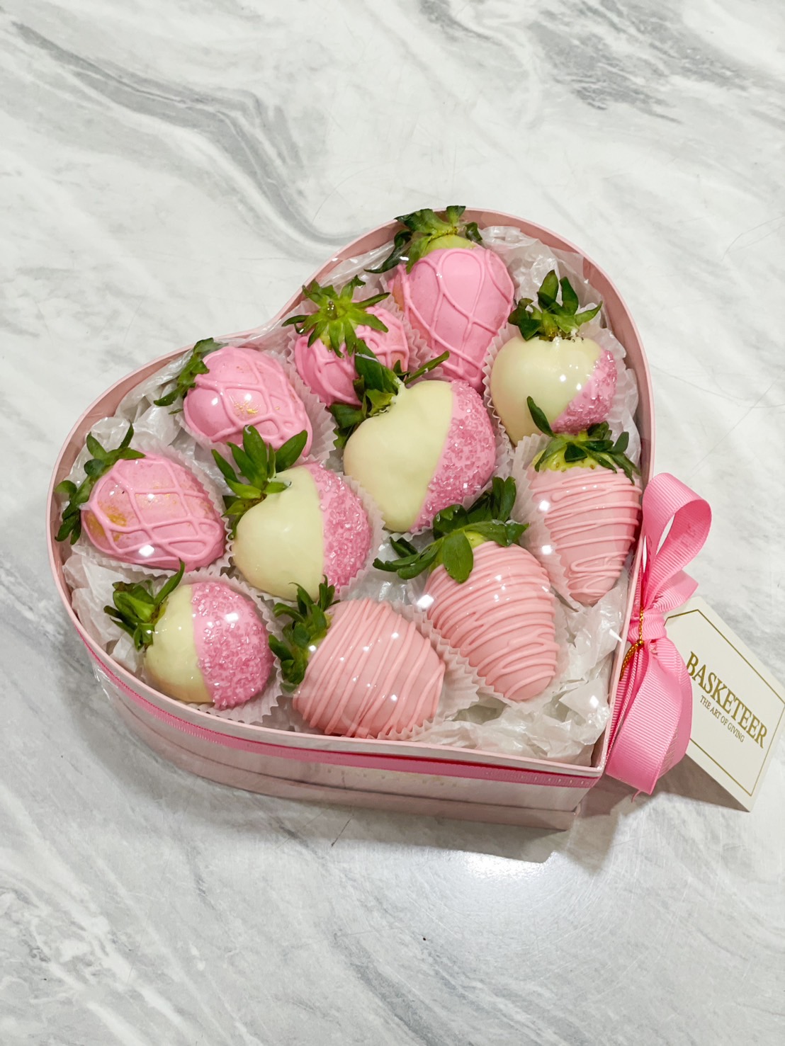 Heart-shaped box of pink and white chocolate-covered strawberries with gold accents, sugar crystals, and delicate drizzles.