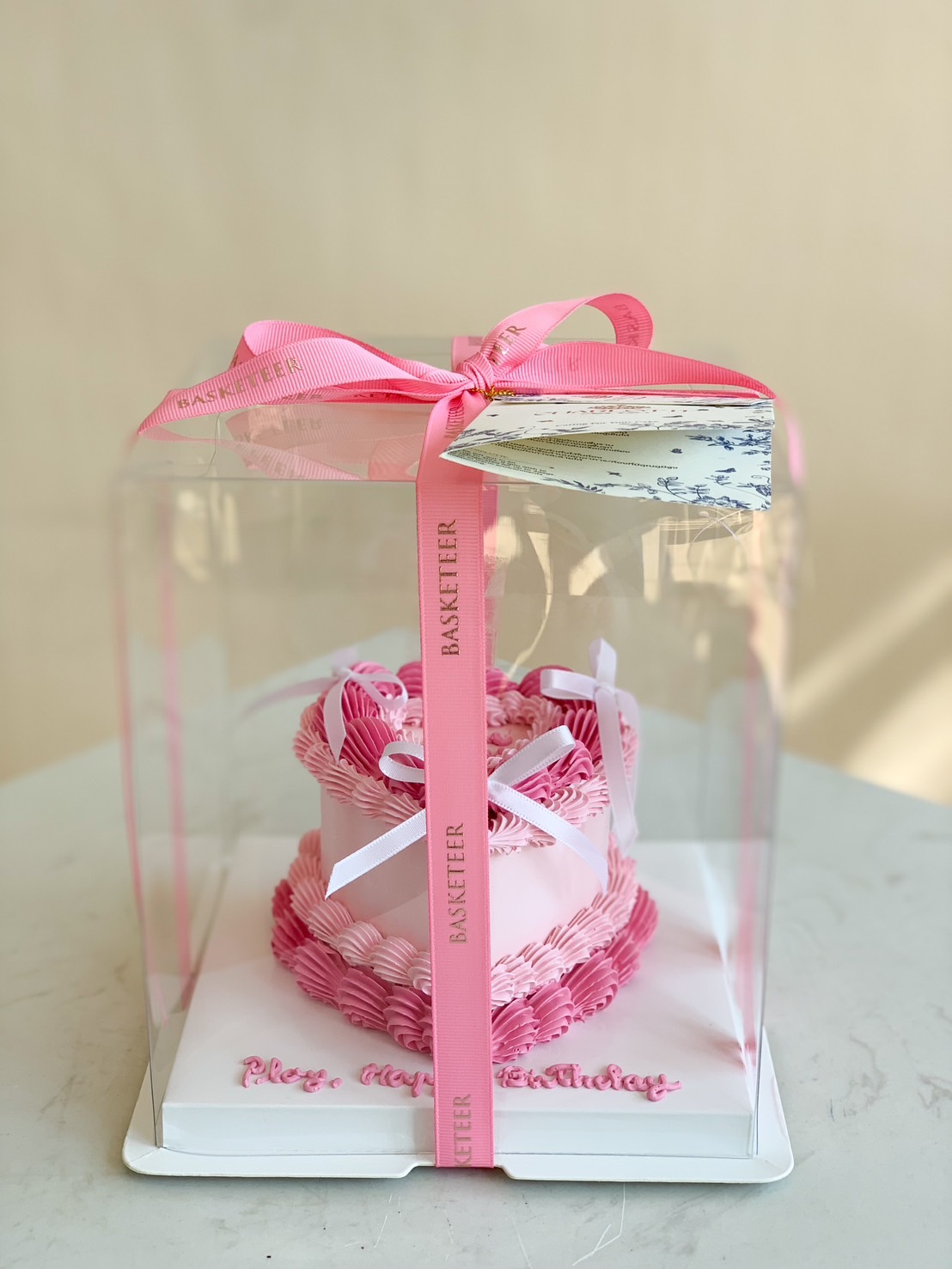 Pink ombre heart-shaped birthday cake with delicate ruffle buttercream frosting, elegantly packed in a clear gift box with a pink satin ribbon.